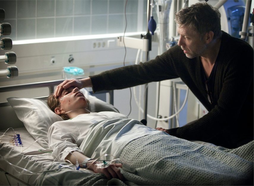 "Der Hypnotiseur": Erik Maria Bark (Mikael Persbrandt) sitzt an Josefs (Jonatan Bökman) Bett im Krankenhaus und legt ihm die Hand auf die Stirn.