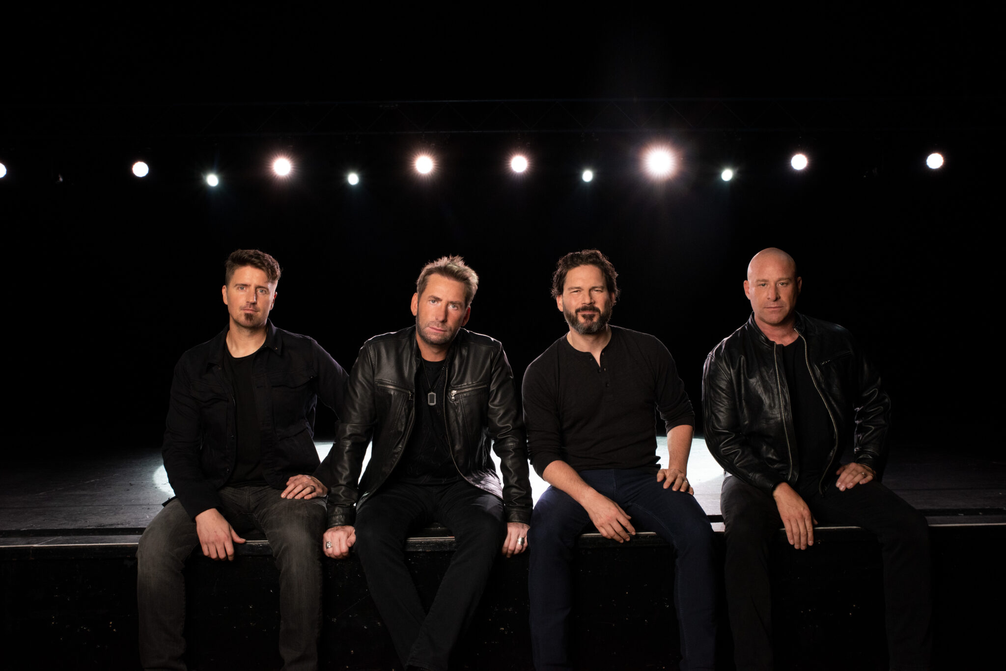 Gruppenportrait Nickelback am Bühnenrand sitzend