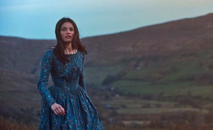 Emma Mackey in einem blauen Kleid in hügeliger Landschaft