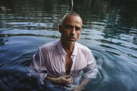 Eros Ramazzotti steht mit einem weißen Hemd in einem See.