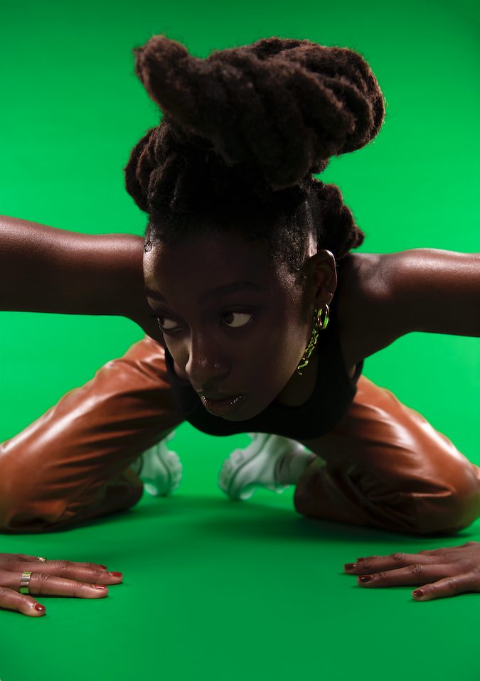 Die Sängerin Little Simz kniet auf einem grünen Fußboden
