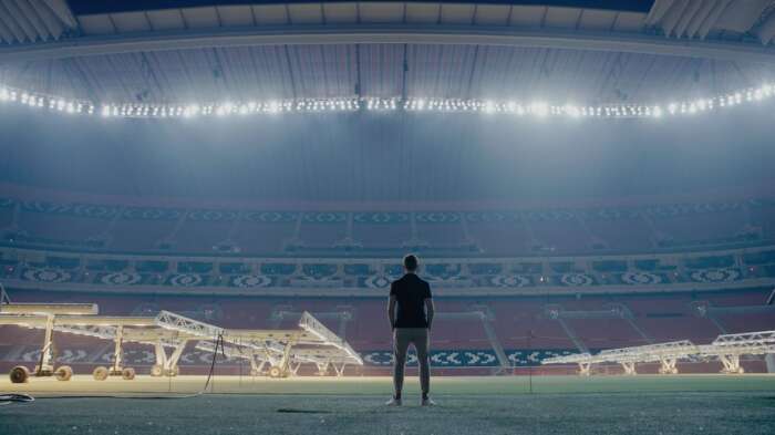 "ZDFzeit: Geheimsache Katar": Blick in ein leeres, hell beleuchtetes Fußballstadion. In der Mitte sind die dunklen Umrisse eines Menschen zu erkennen, der dem Betrachter den Rücken zukehrt