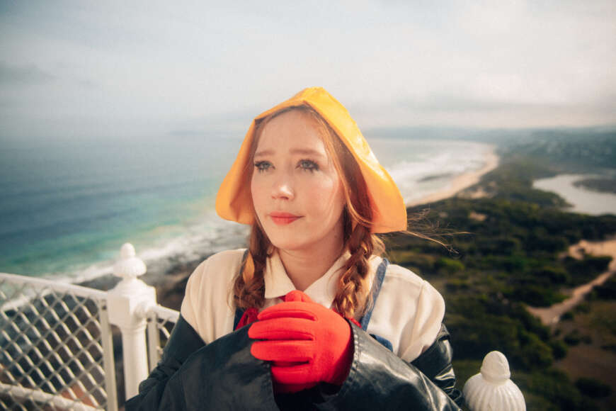 Julia Jacklin steht auf einer Terrasse mit einem roten Handschuh an und einer gelben Haube auf dem Kopf.