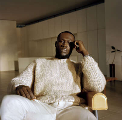 Stormzy sitzt auf einem Sessel und schaut in die Kamera.