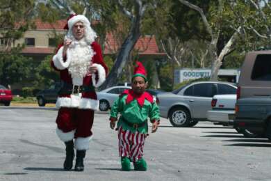 "Bad Santa": Willie T. Stokes (Billy Bob Thornton) und Marcus (Tony Cox) laufen nebeneinander auf einem Parkplatz entlang und unterhalten sich. Die beiden sind als Weihnachtsmann und Elf verkleidet.
