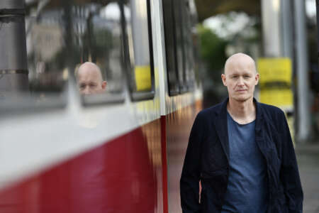 Portraitfoto Arno Geiger, aufgenommen auf Bahnsteig, spiegelt sich im Zugfenster