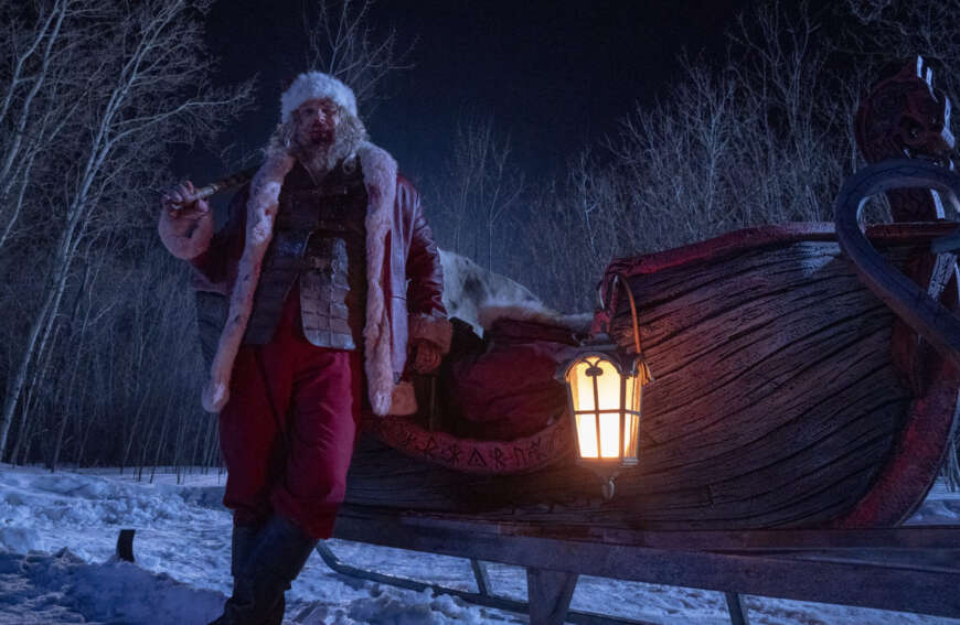 David Harbour als Weihnachtsmann steht vor einem Schlitten.