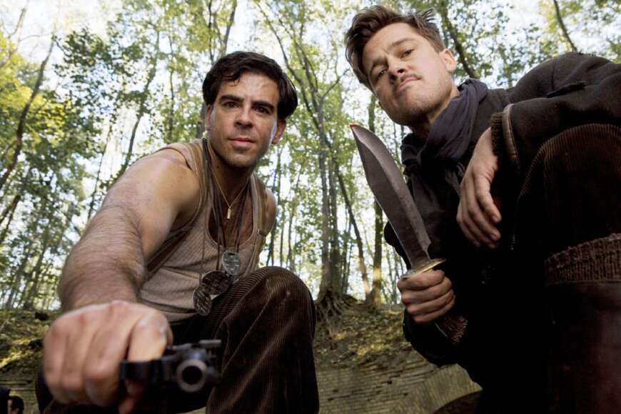 „Inglourious Basterds“: Sgt. Donny Donowitz (Eli Roth, l.) und Leutnant Aldo Raine (Brad Pitt) knien auf dem Boden und schauen direkt in die Kamera. Horowitz hat eine Pistole in der Hand, Raine ein Messer.