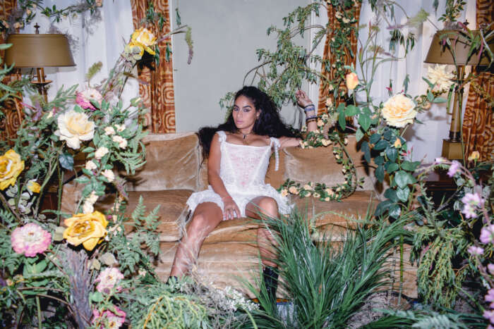 Klub-Highlights: Jessie Reyez sitzt auf einem Sofa, umringt von Pflanzen.