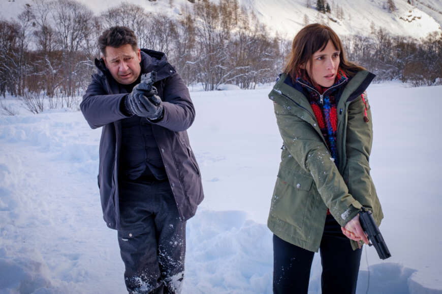 "Schwarz wie Schnee": Constance Vivier (Clémentine Poidatz) auf der Rechten und Andreas Meyer ( Laurent Gerra) auf der Linken. Im Hintergrund eine Schneelandschaft. Beide haben ihre Waffe in der Hand und zielen auf eine Person außerhalb des Bildes.