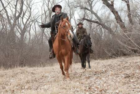 "True Grit": Rooster Cogburn (Jeff Bridges) sitzt auf einem braunen Pferd und blickt in die Ferne. Hinter ihm reitet Mattie Ross (Hailee Steinfeld) auf einem schwarzen Pferd.