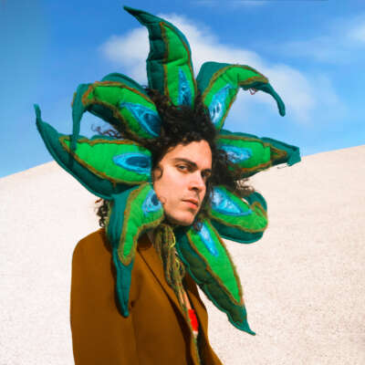Alex Vargas ist mit Blumenmaske um den Kopf vor einer Sanddüne zu sehen.