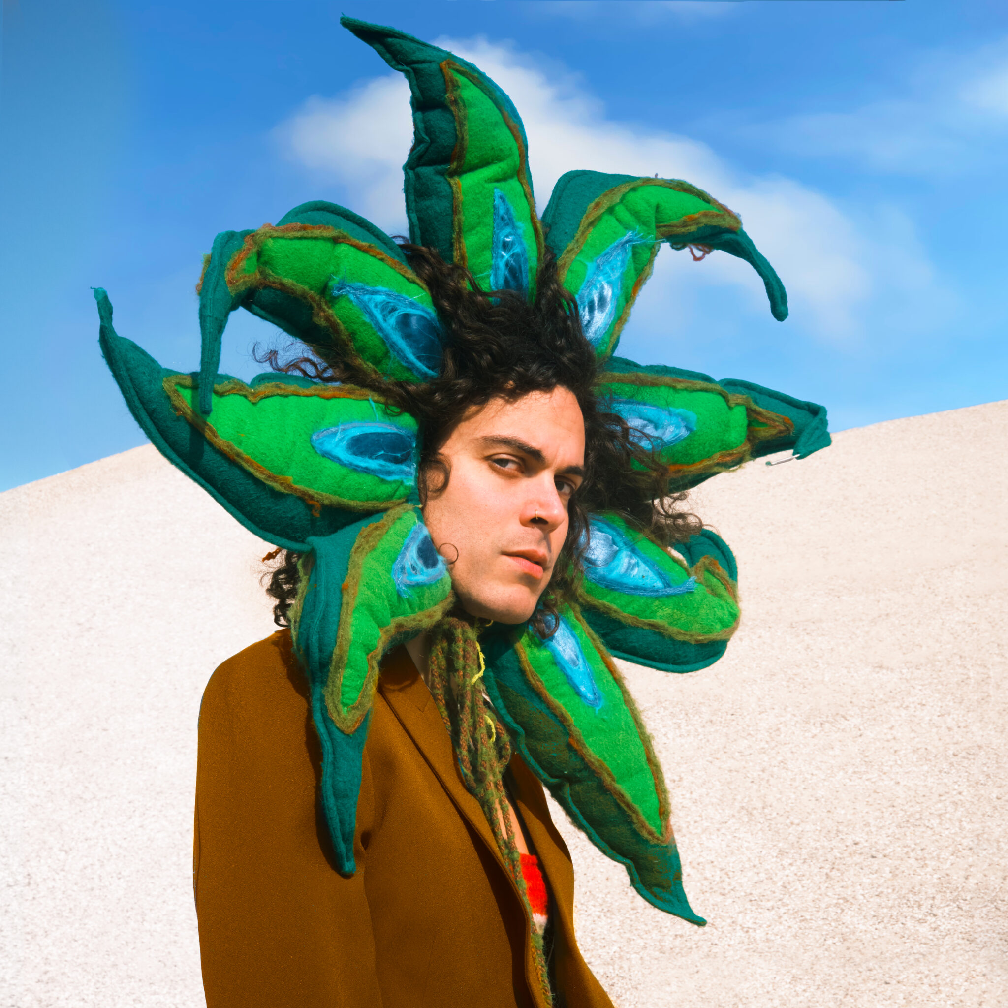 Alex Vargas ist mit Blumenmaske um den Kopf vor einer Sanddüne zu sehen.