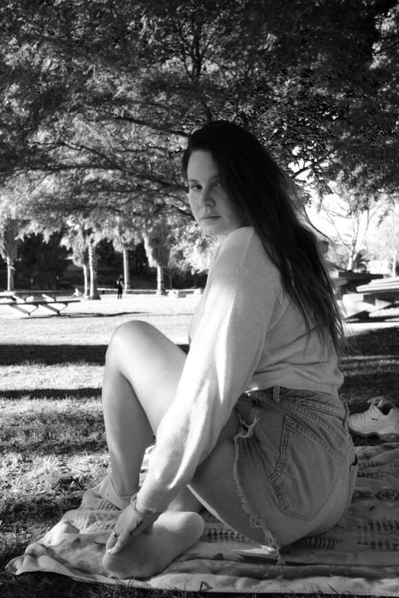Lana Del Rey sitzt auf einer Decke im Park.