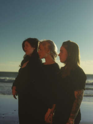 Lucy Dacus, Phoebe Bridgers und Julien Baker stehen am Strand, im Hintergrund das Meer.