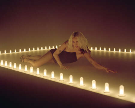 Miley liegt auf einem Podest umgeben von Kerzen.