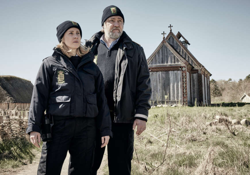 „Der Dänemark-Krimi: Blutlinie“: Streifenpolizisten Ida (Marlene Morreis) und Magnus (Nicki von Tempelhoff) stehen auf einer Wiese vor einer alten Kirche.