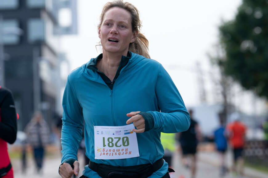 "Laufen": Juliane (Anna Schudt) joggt in einer blauen Laufjacke, mit einer vierstelligen Startnummer auf dem Bauch, auf einer Straße entlang.