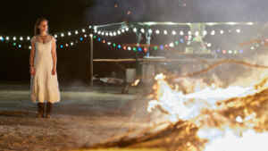 Still aus „Ostfriesenfeuer“: Ann Kathrin Klaasen (Picco von Groote) steht nachts im Brautkleid am Strand. Im Vordergrund rechts brennt ein Osterfeuer.