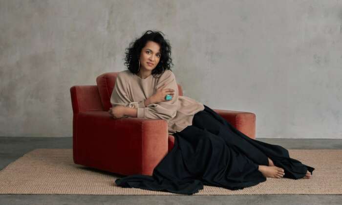 Anoushka Shankar, auf einem roten Sessel. vor einem grauen Hintergrund, sitzend.