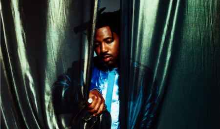 Sampha, halb hinter einem grünen Vorhang stehend.