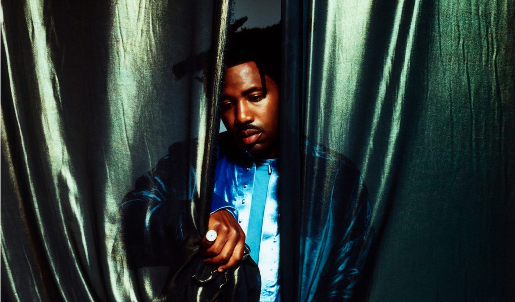 Sampha, halb hinter einem grünen Vorhang stehend.