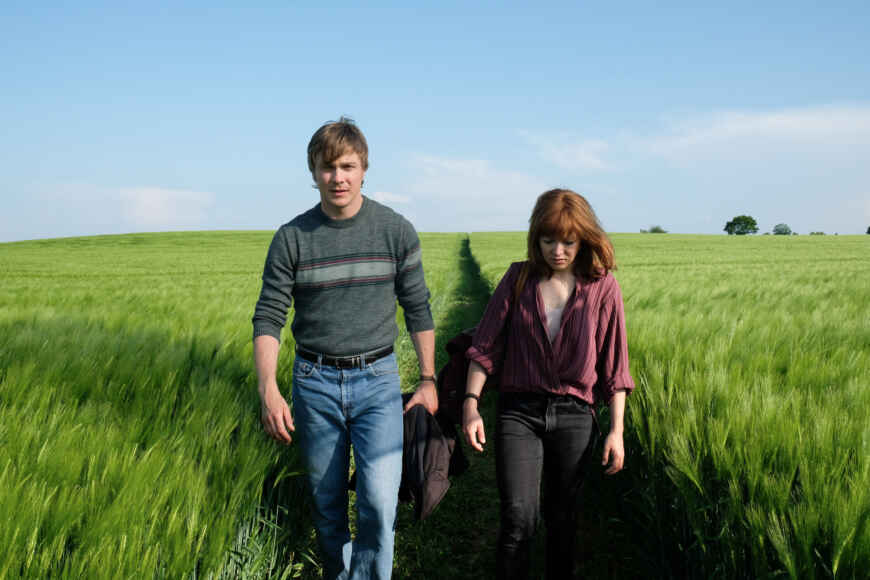 "Verräter - Tod am Meer": Martin (Albrecht Schuch) und Nina (Hannah Herzsprung) laufen nebeneinander durch ein grünes Feld.