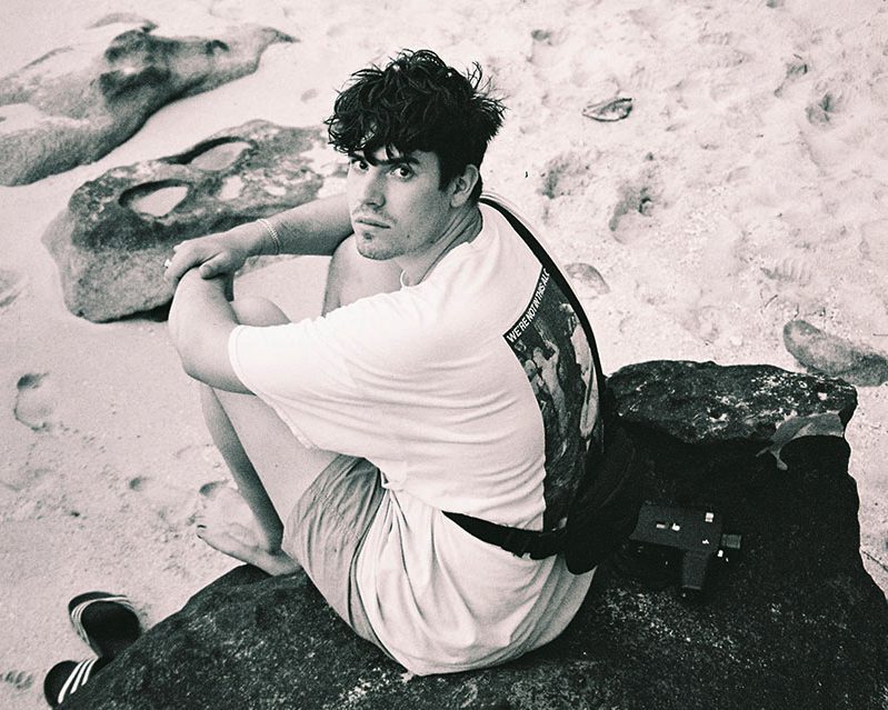 Edwin Rosen auf einem Stein am Strand sitzend. Schwarz/Weiß Fotografie.