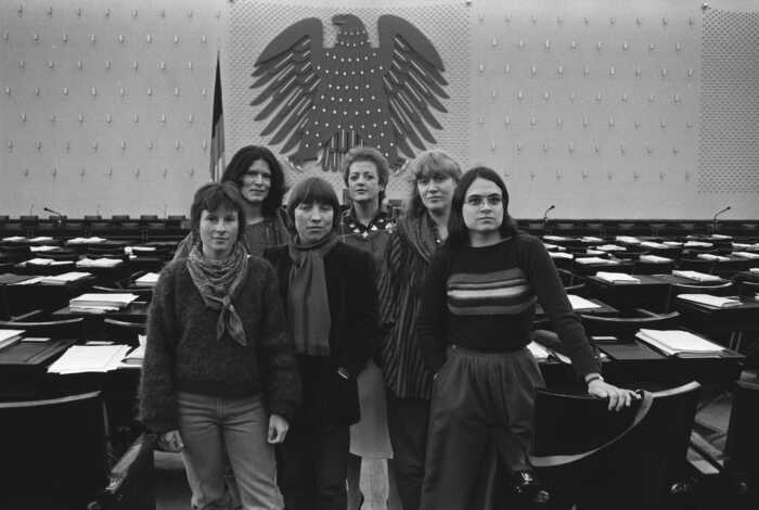 "Die Unbeugsamen": SW-Fotos von 1984: eine Gruppe von sechs Frauen steht zusammen, im Hintergrund die leeren Abgeordnetentische und Regierungsband des deutschen Bundestages in Bonn. Es sind die Sprecherinnen der Fraktion der Partei Die Grünen.