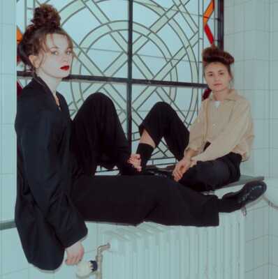 Das Duo Kids With Buns auf einer Fensterbank, vor einem Fenster, sitzend.