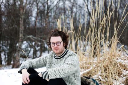 Zach Condon, Frontmann von Beirut, in einem schneebedeckten Wald sitzend.