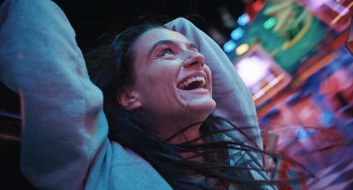 "Zwischen uns die Nacht": Marie (Laura Balzer) lacht glücklich und hat die Arme nach oben gehoben. Ihre Haare fliegen wild umher. Im Hintergrund sind die bunten Lichter des Jahrmarkts zu sehen.