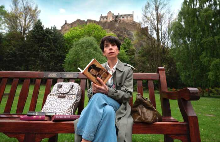The lost King Ein Frau mit kurzen schwarzen Haaren sitzt auf einer Parkbank und liest ein Buch