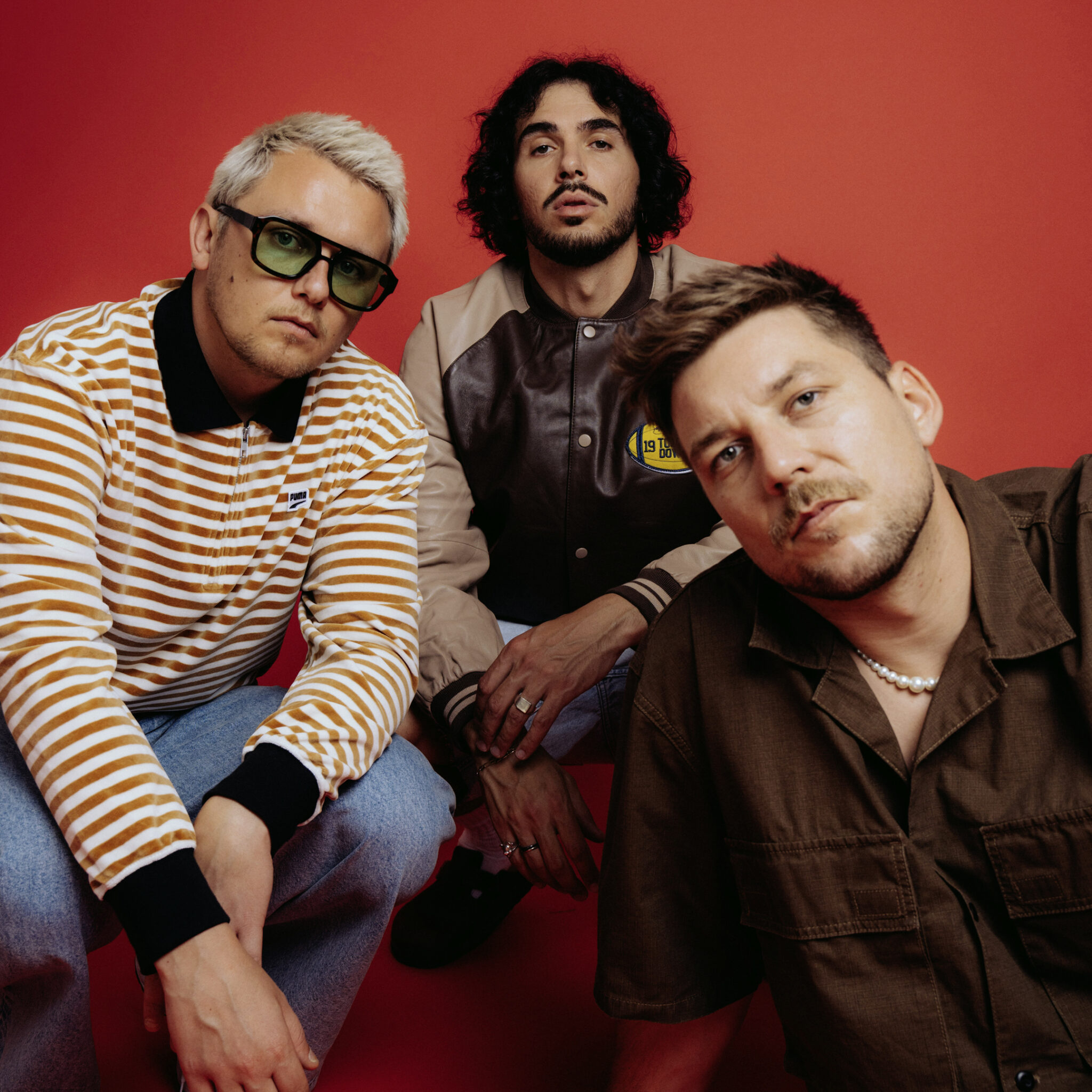 Das Electropop-Trio ClockClock sitzt vor einem roten Hintergrund.