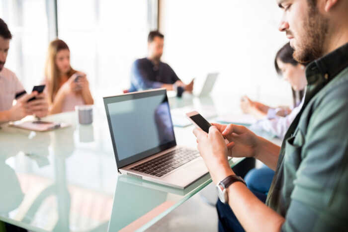 young-handsome-latin-man-sitting-conference-table-using-mobile-phone-with-colleagues-sitting-by