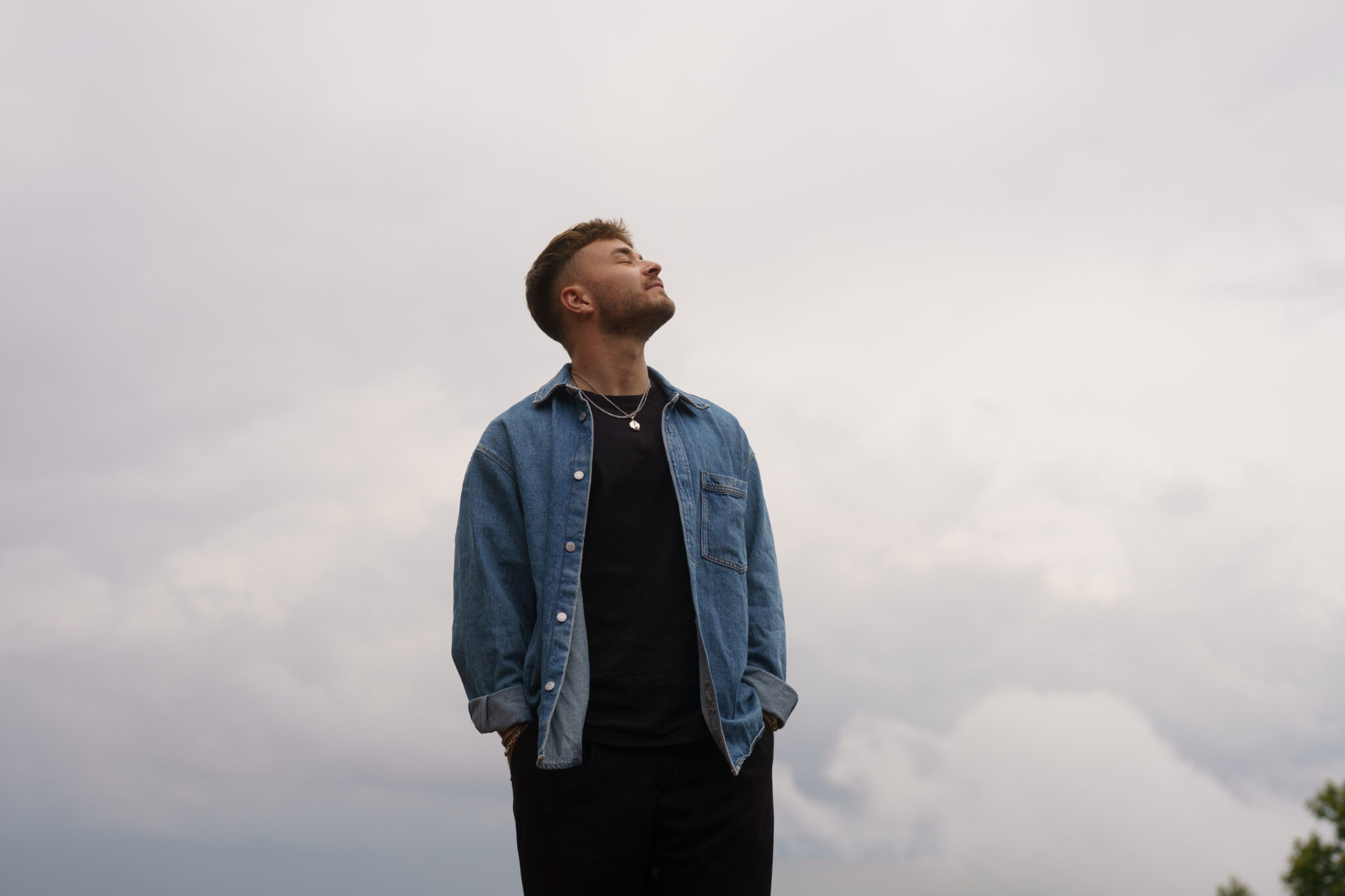 Pressebild Julian Pfoertner: Julian Pfoertner steht vor einem grauen Himmel und schaut nach oben