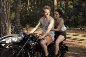 Still aus „In Liebe, eure Hilde“: Hans und Hilde Coppi sitzen lächelnd auf einem Motorrad.