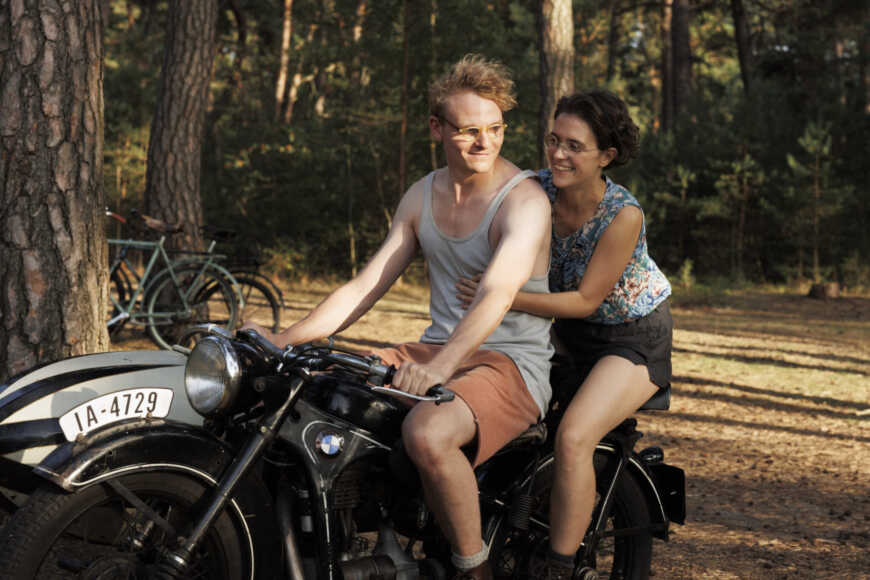 Still aus „In Liebe, eure Hilde“: Hans und Hilde Coppi sitzen lächelnd auf einem Motorrad.