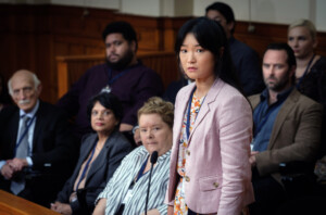 Einige Geschworene sitzen auf einer Bank im Gerichtssaal, im Vordergrund die asiatischstämmige Protagonistin.