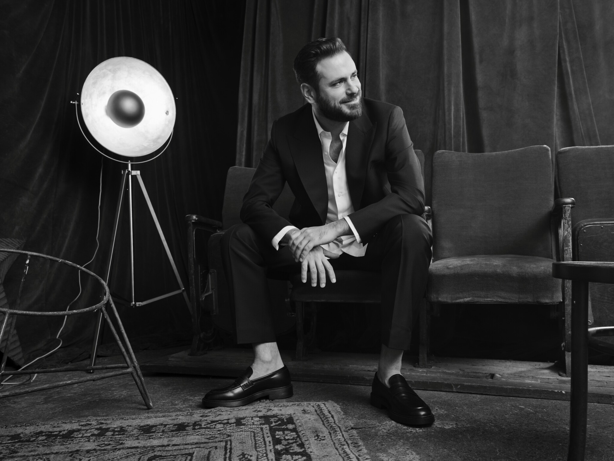 Schwarzweiß-Foto: Der Musiker sitzt auf einer Couch und blickt lächelnd zur Seite, neben ihm steht ein altmodischer Scheinwerfer