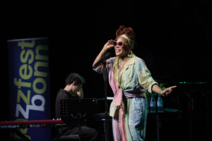 China Moses steht im Overall auf der Bühne und singt.
