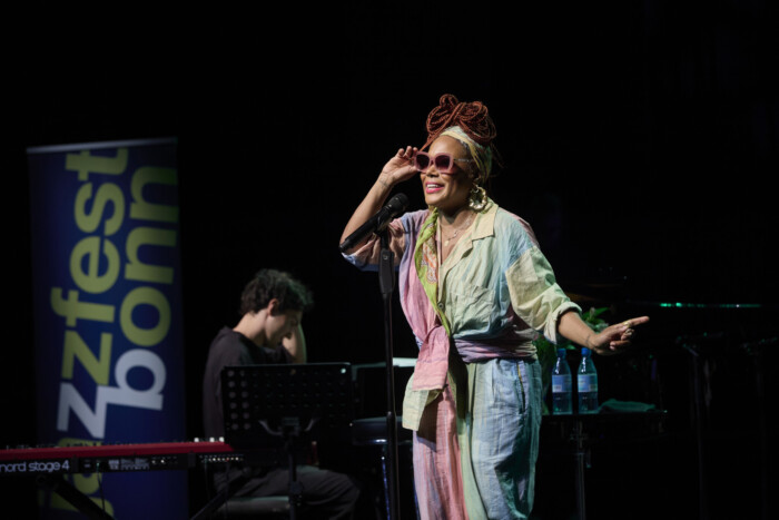 China Moses steht im Overall auf der Bühne und singt.