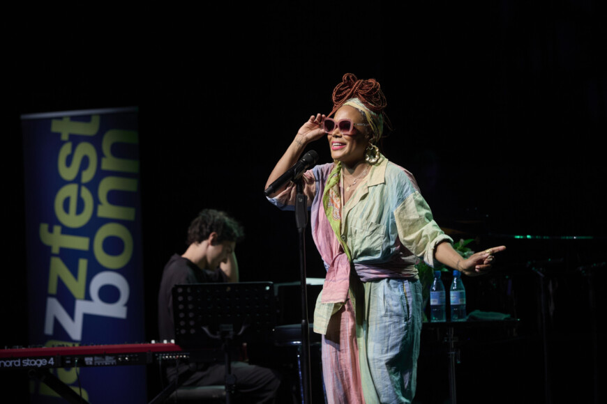 China Moses steht im Overall auf der Bühne und singt.