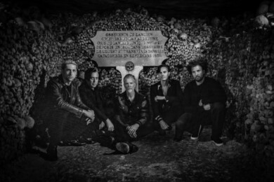 Ein Schwarz-Weiß-Foto zeigt die fünfköpfige Band kniend und sitzend vor einer Wand aus Knochen und Totenschädeln.