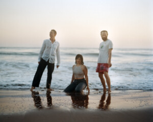 Die Band in Sommerklamotte am Strand nah beim Wasser.