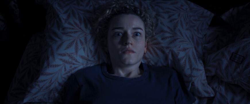 Still as „Weapons“: Justine (Julia Garner) liegt auf dem Rücken im Bett und starrt erschrocken nach oben.