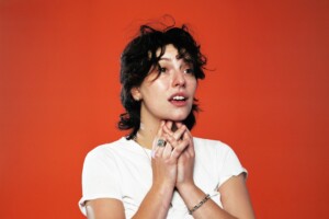 King Princess steht vor rotem Hintergrund und sieht verheult aus.