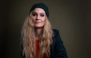 Anika Nilles steht vor einem einfarbigen Hintergrund, trägt eine Mütze und schaut in die Kamera.