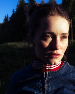 Sigrid steht in der Natur und schaut an der Kamera vorbei in die Sonne.