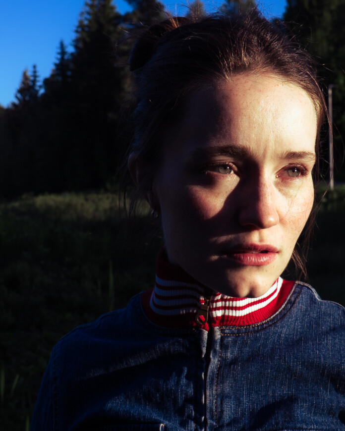 Sigrid steht in der Natur und schaut an der Kamera vorbei in die Sonne.